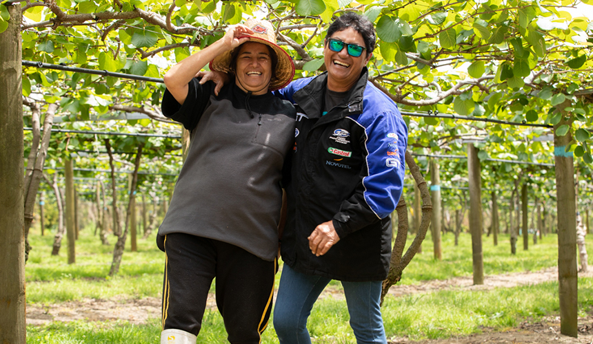 Two people laughing together, standing in an orchard.