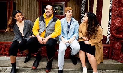 Four people laughing and talking at the entrance to a marae.