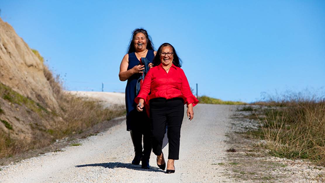 Two women walking down a road laughing together.