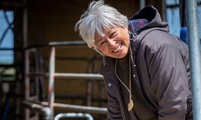 A woman smiling at the camera, standing at the endtrance to a farm building.