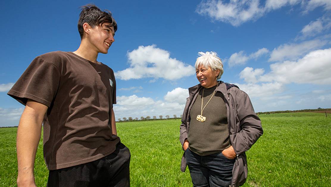 Two people smiling together, standing outside in a field.