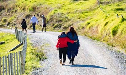 Two women walking away along a road with their arms around each other.